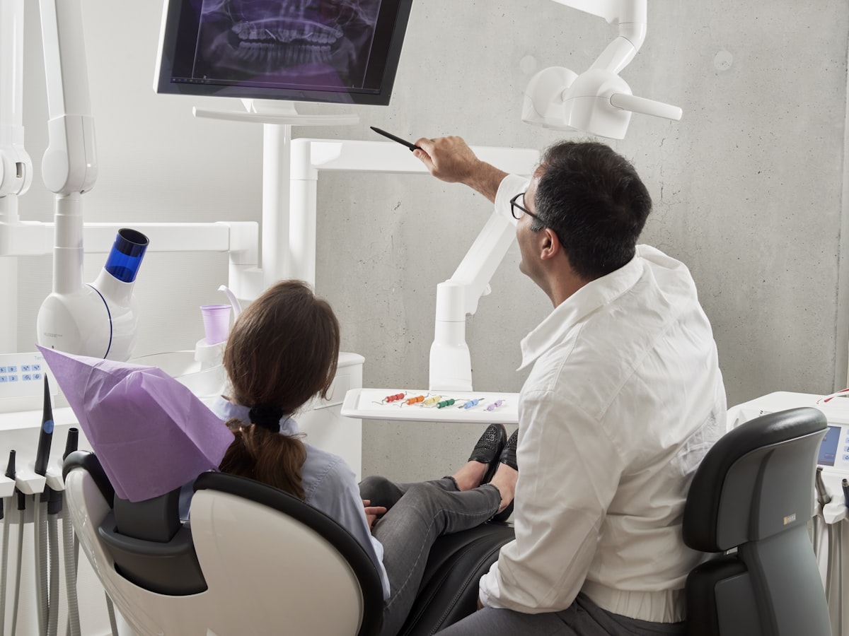 A dentist showing a patient her X-ray on a screen beside the chair